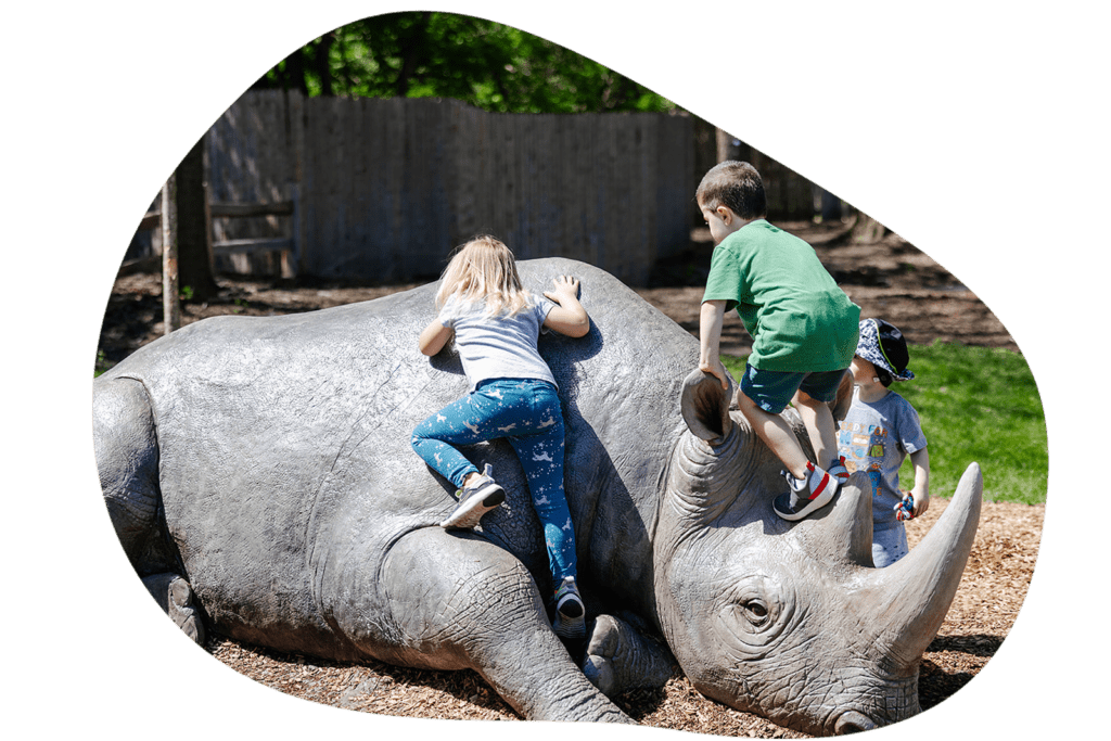 Three children climb on top of a life-sized sculpture of a black rhino.